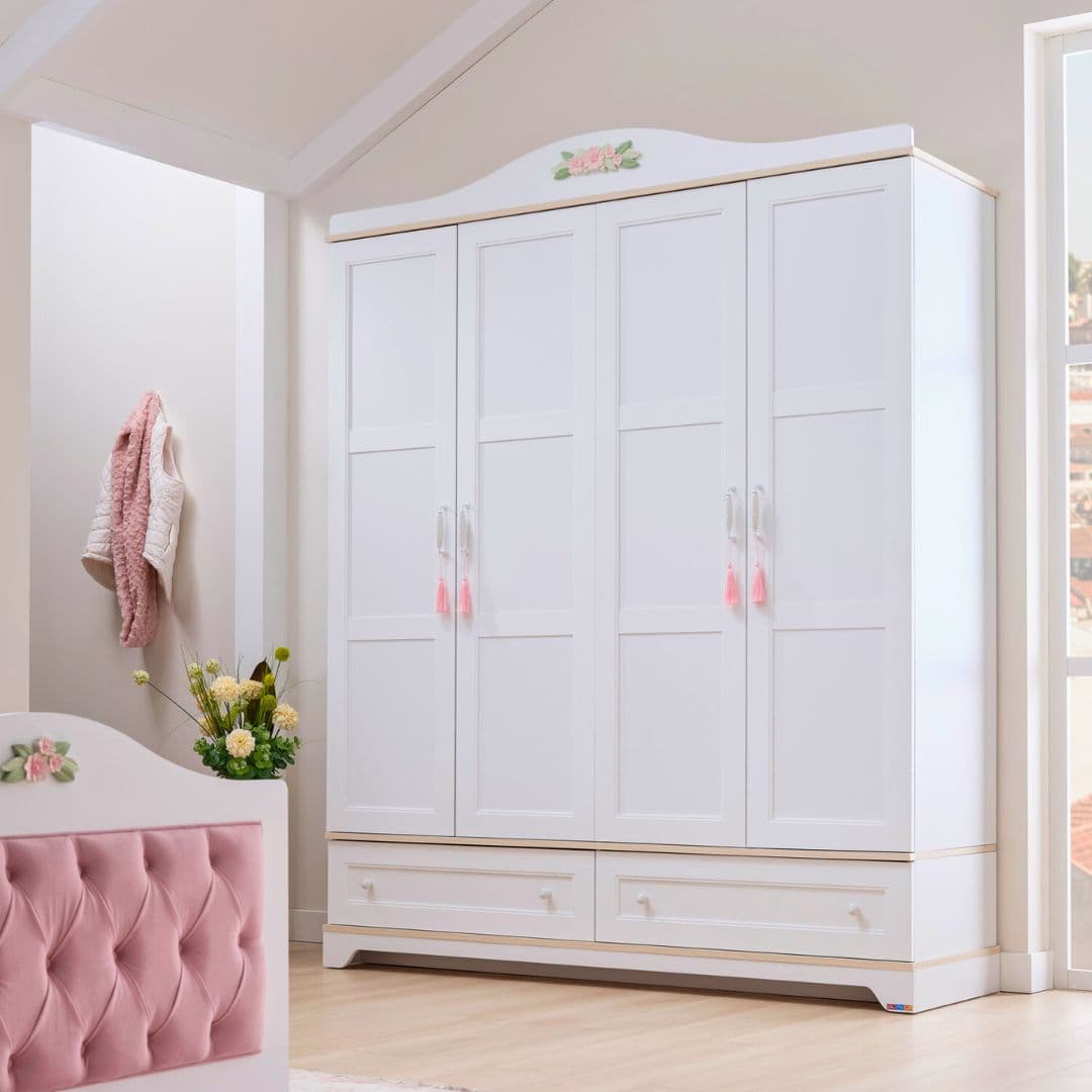 Детски гардероб Bianca в стая – бял гардероб с 4 панелни врати и декоративно керамично цвете отгоре. Стои нежно и светло в интериора.